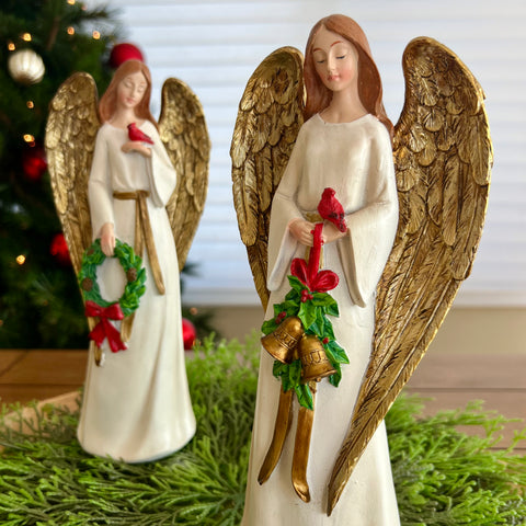 Two angel figurines with gold wings holding Christmas decorations in front of a blurred festive background.