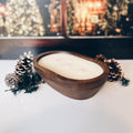 Wooden bowl with a white candle on a snowy surface, Christmas trees in the background