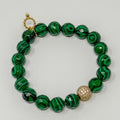 Green beaded bracelet with a gold charm on a light gray background