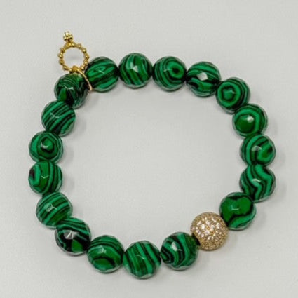 Green beaded bracelet with a gold charm on a light gray background